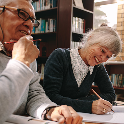 a senior man and woman writing in journals at the library inside of their senior living community