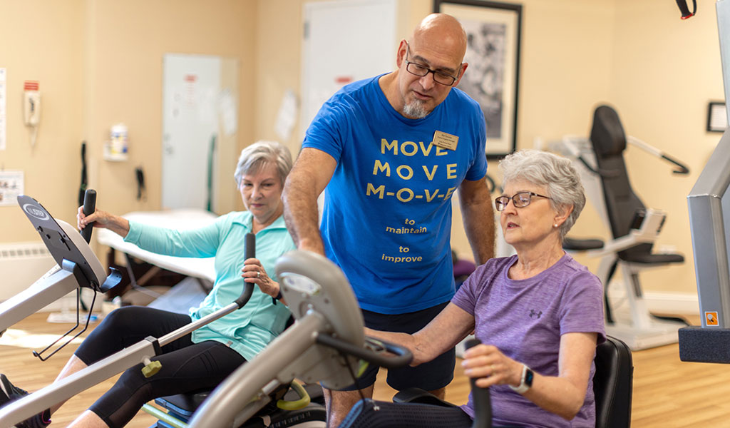 Two resident women working with a trainer in the fitness center at Lake Forest Place