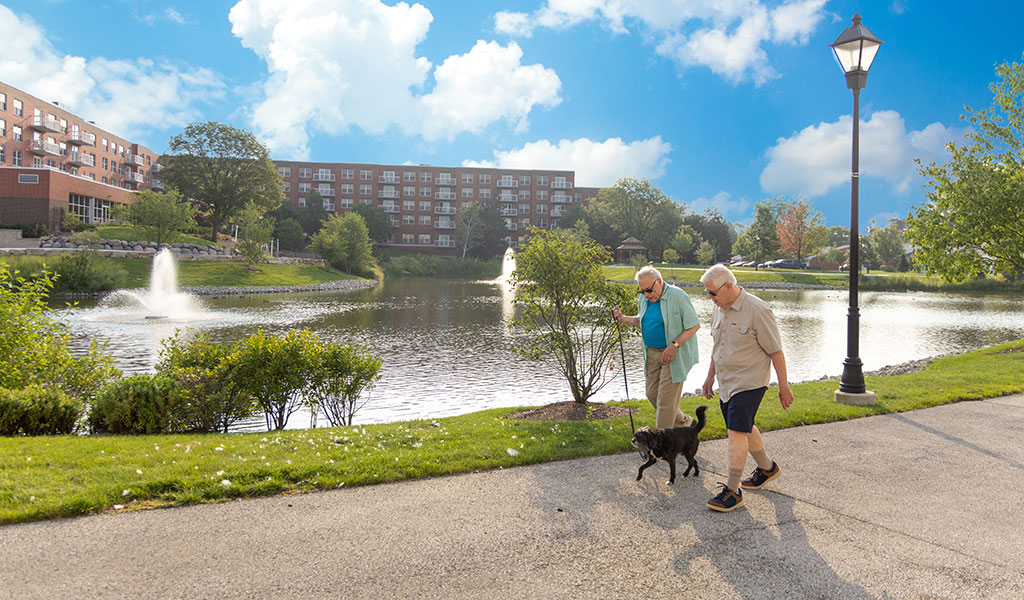 Resident couple walking their dog near beautiful fountains at The Moorings of Arlington Heights