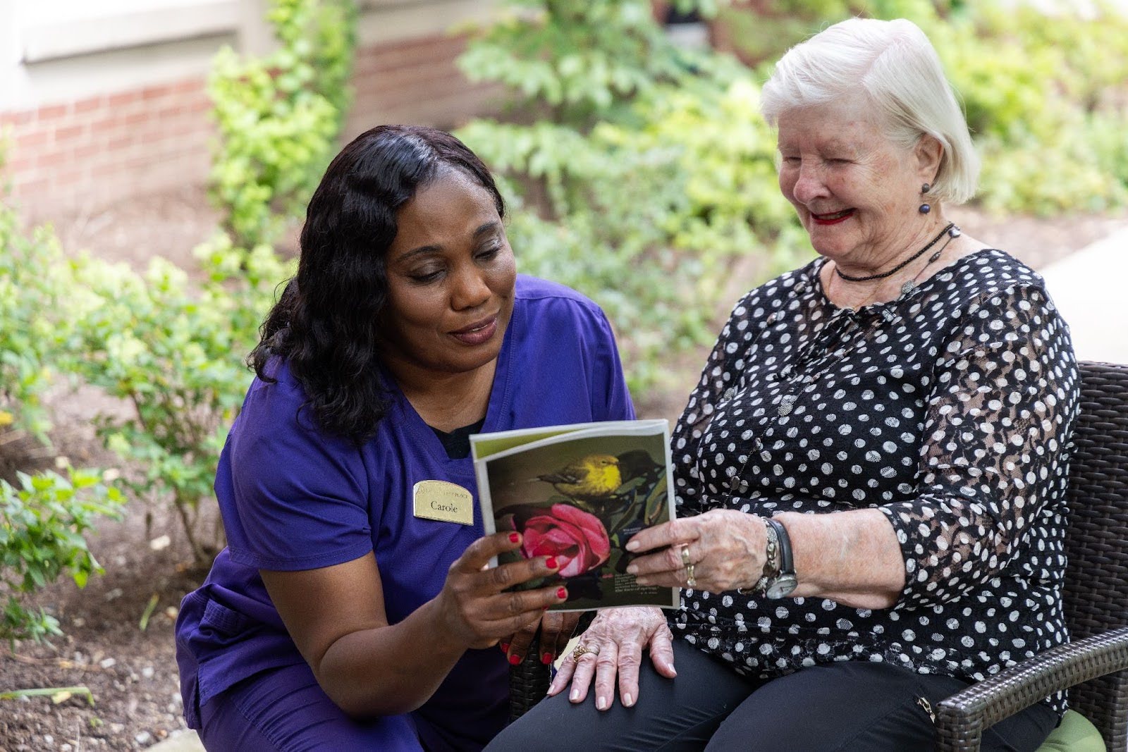 Resident at Lake Forest Place reading outdoors with her caregiver