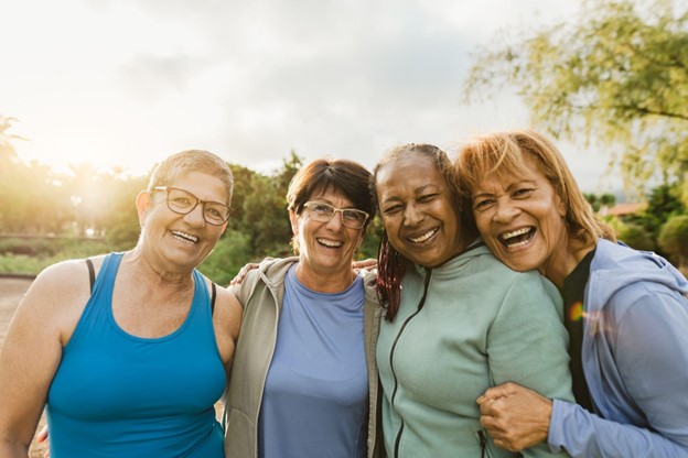 a group of senior women in fitness clothing laughing together outside as the sun sets