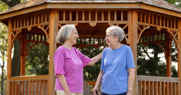 two senior women standing in front of a wooden gazebo