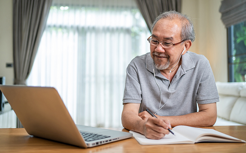 Senior man taking notes while attending a virtual learning session on his laptop