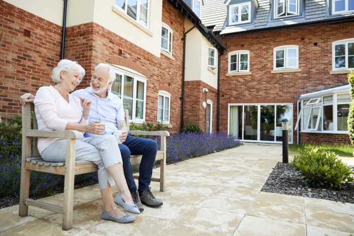 a senior couple sitting on a bench outside their senior living community