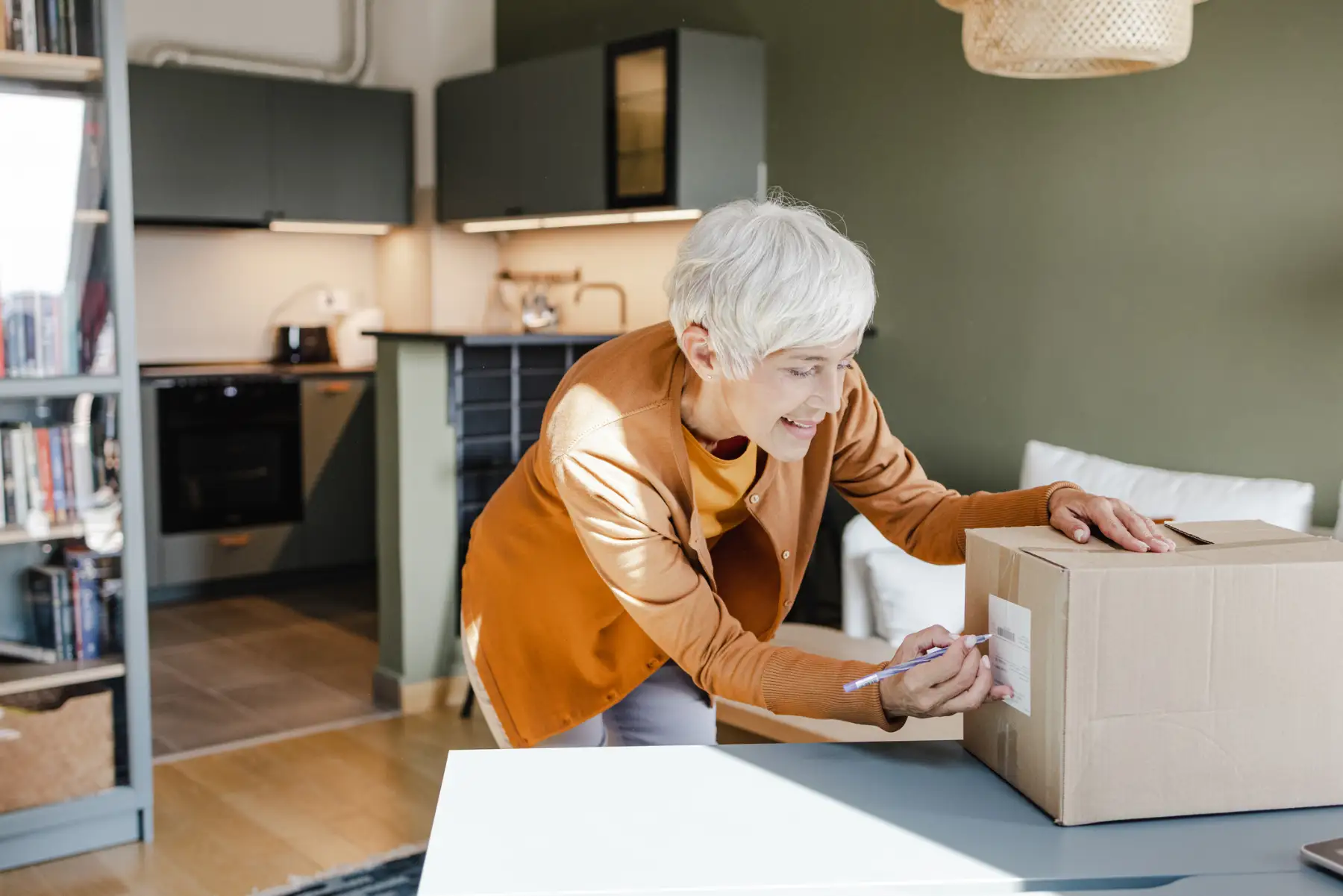 a senior woman writing on the label of a moving box